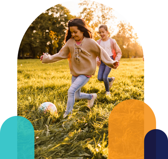 Zwei Kinder spielen Fußball auf einer Wiese im warmen Abendlicht.